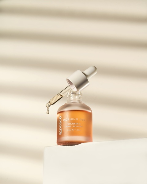 A high-end studio shot of a Vitamin C serum bottle with a dropper, utilizing natural-looking shadow overlays to convey purity and morning radiance.